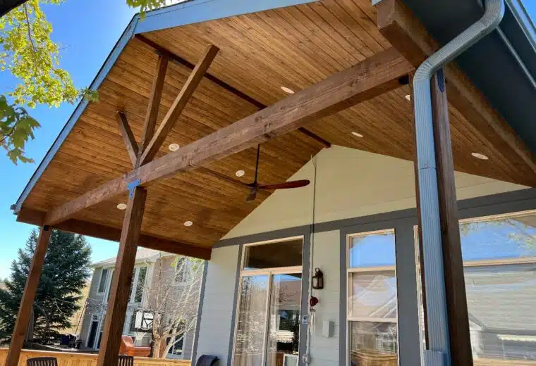 Gable patio cover with a stained wood ceiling, exposed beams and a ceiling fan