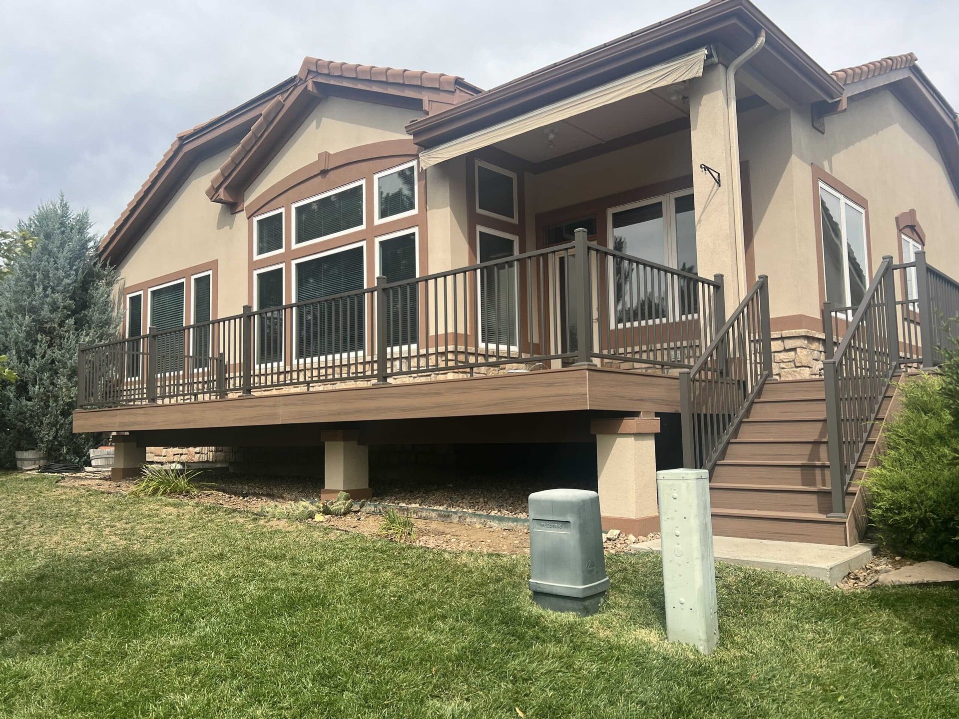 Composite deck with bronze aluminum railing wrapping a stucco home, with stairs down to the lawn