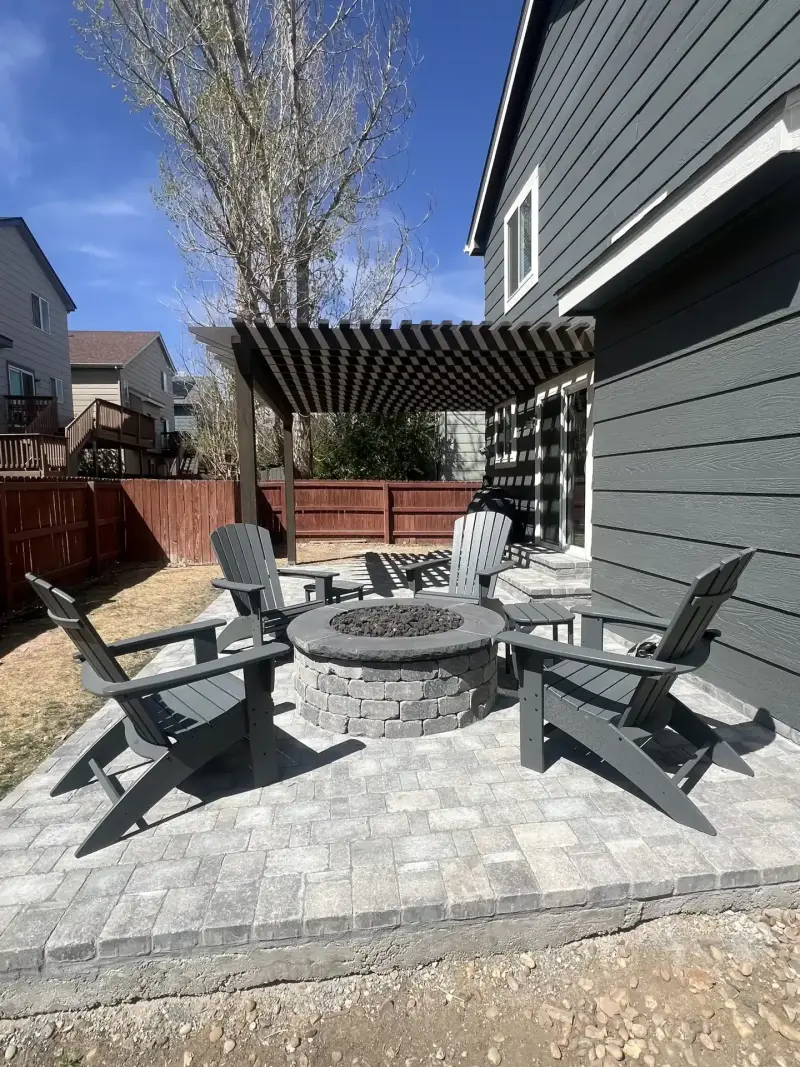 Paver patio with a stone fire pit and Adirondack chairs under a pergola