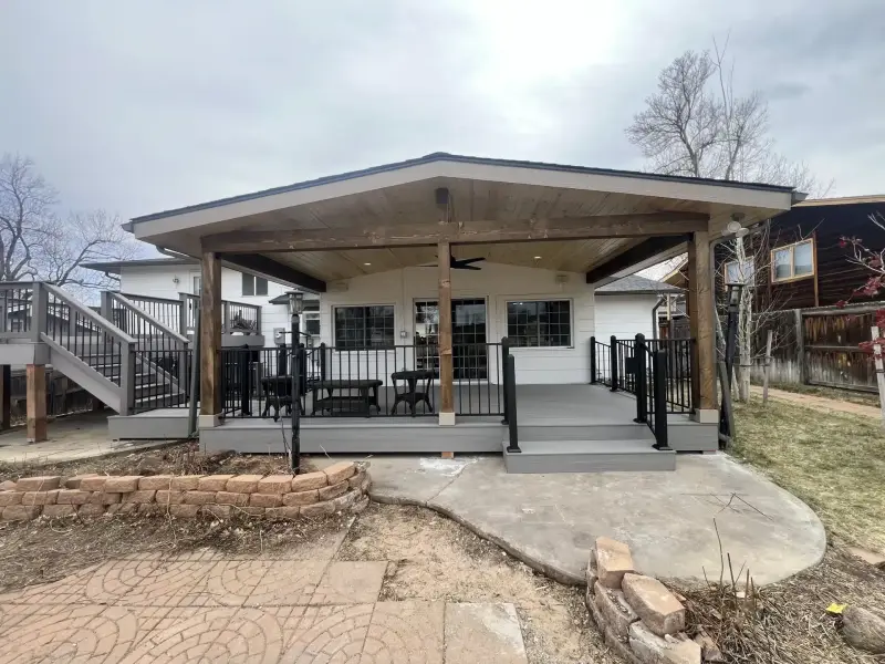Composite deck with black metal railing under a gable patio cover with wood beams